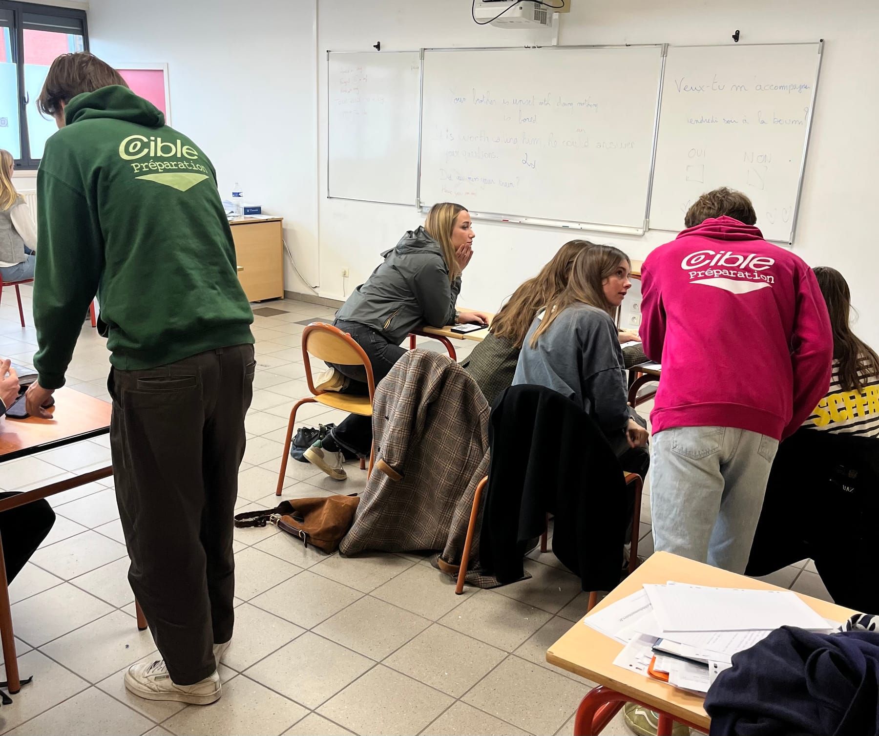 Cours en petit groupe : deux cibleurs en sweat Cible penchés vers des élèves au travail